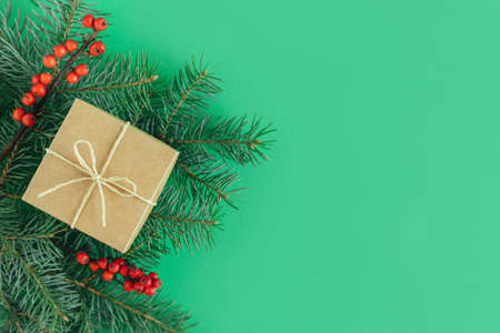 Craft gift box with spruce branch and red berries on a green background. Holiday concept. Place for text. Flat lay.の写真素材