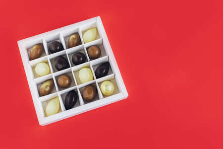 Gift box with chocolate candies on a red background. Holiday concept. Place for text. Flat lay.