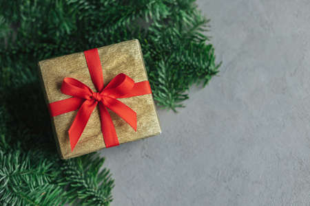 Gift box with red ribbon on a green spruce background. Holiday concept. Place for text. Flat lay.