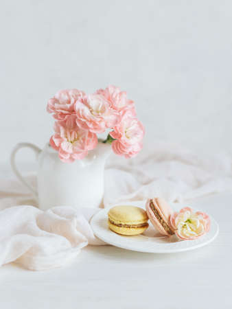 Two tasty French macarons and a jar with pink carnation flowers on a white background. pastel...