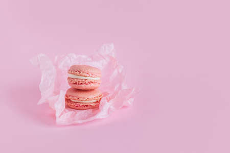Tasty french macaroons with flowers on a pink pastel background. Place for text.