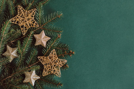 Spruce branches with golden sparkling stars on a dark green background. Flat lay. Place for text.