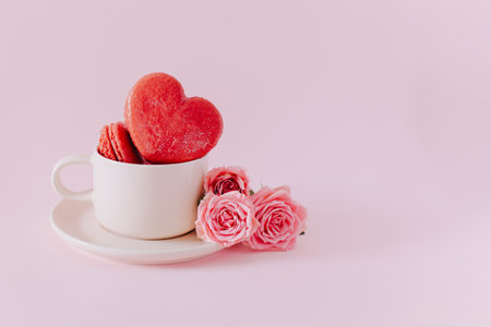 Pink heart shaped French macarons with rose flowers on a pink pastel background. Concept for Valentine's day. Place for text.の写真素材