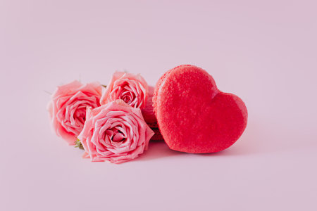 Pink heart shaped French macarons with rose flowers on a pink pastel background. Concept for Valentine's day. Place for text.の写真素材