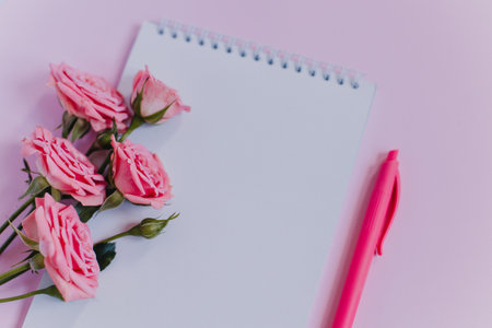 Notebook with blank page and rose flowers on pink background. Flat lay. Place for text.の写真素材