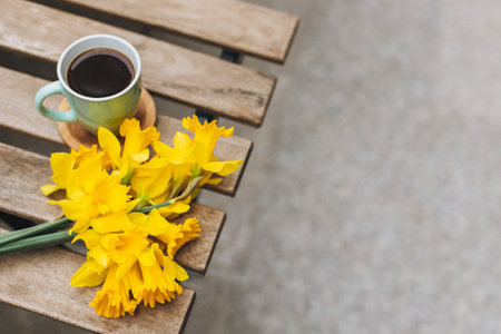 Cup of black coffee and bouquet of yellow daffodils (narcissus) on a wooden table in a street cafe. Place for text.の写真素材