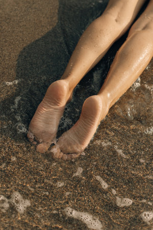 Women's feet in the sea. Close-up top view of a young woman's bare feet in a water on a beach.の写真素材