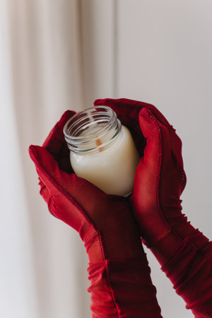 Female hands in dark red gloves holding tender white candle. Close up.の写真素材