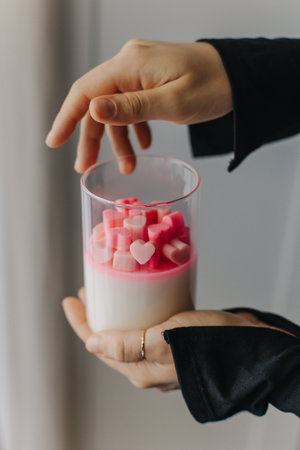 Female hands holding a glass with pink heart-shaped objects. Close up.の写真素材