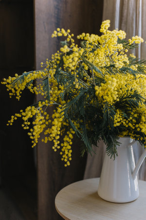 Beautiful Mimosa flowers in a white jar on table Cozy home atmosphere. Selective focus.の写真素材