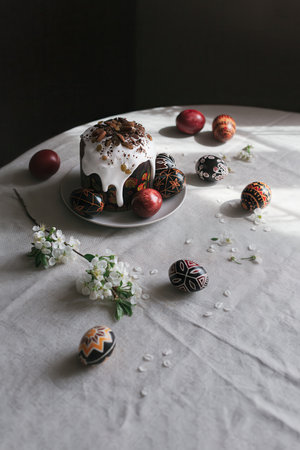 Traditional Ukrainian Easter bread Paska and easter eggs Pysanka in black, red and white colors with cherry blossom on a table. Easter still life. Modern minimalism.の写真素材