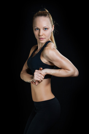 Athletic young woman showing muscles arms on a isolated black backgroundの写真素材