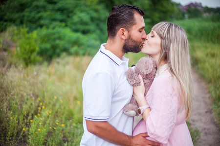 man and pregnant woman outdoor embracing kissing among them a soft toy teddy bearの写真素材