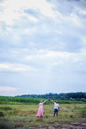 man and pregnant woman on nature on the background of the night sky are keeping hands up with teddy bearの写真素材