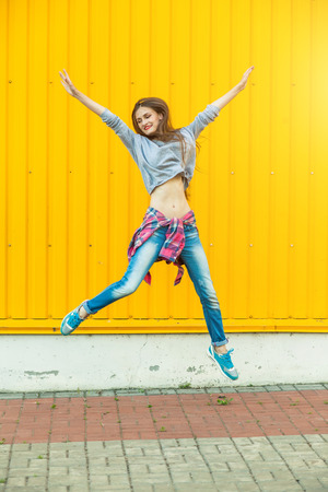 Trendy Beautiful long haired Young Woman having fun and jumping on bright Yellow Backgroundの写真素材