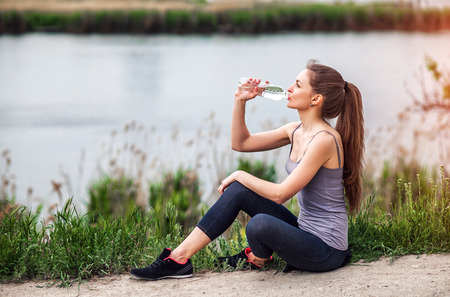 Attractive Sporty Young Woman drinking Water from a bottle after jogging or runningの写真素材