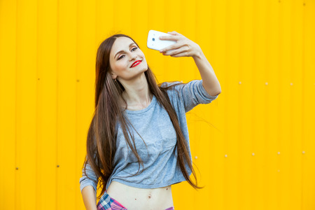 Outdoor portrait of beautiful girl taking a selfie with mobile phone in cityの写真素材