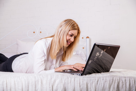 A smiling woman lying down the bed in front of her laptop with her legs raised slightlyの写真素材