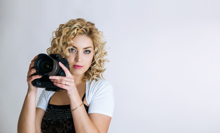 Photographer girl shooting images in studio. Attractive blonde woman taking photos with cameraの写真素材