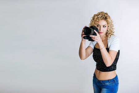 Photographer girl shooting images in studio. Attractive blonde woman taking photos with cameraの写真素材