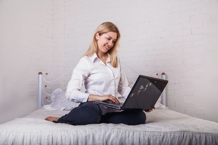 A smiling woman lying down the bed in front of her laptop with her legs raised slightlyの写真素材