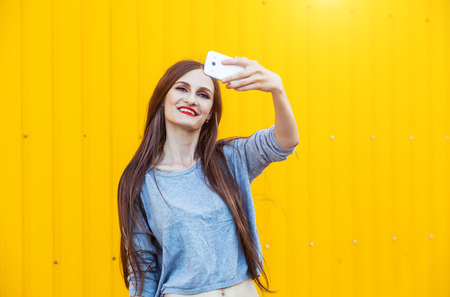 Outdoor portrait of beautiful girl taking a selfie with mobile phone in cityの写真素材