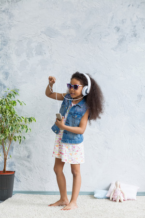 cute African girl at home, listening to music in big white headphones and dancingの写真素材