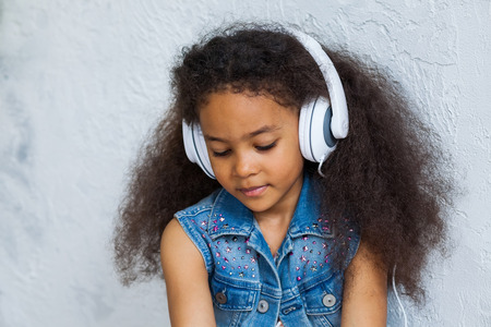 Pretty African girl at home, listening to music in big white headphonesの写真素材