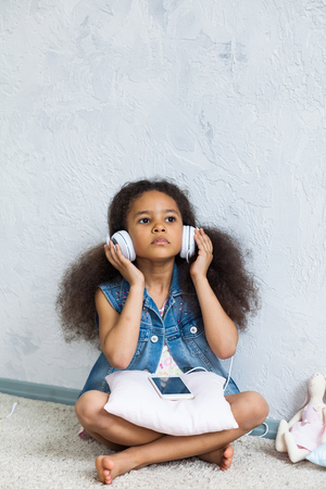 cute African girl at home, listening to music in big white headphonesの写真素材