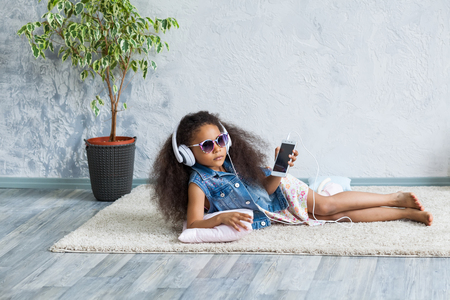 cute African girl at home, listening to music in big white headphonesの写真素材