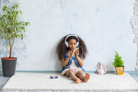 cute African girl at home, listening to music in big white headphonesの写真素材