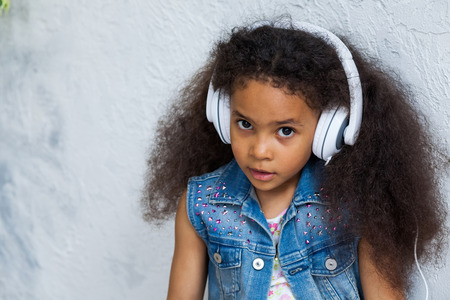 cute African girl at home, listening to music in big white headphones, looking at cameraの写真素材