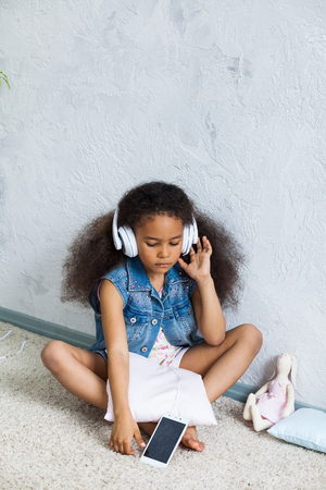 cute African girl at home, listening to music in big white headphonesの写真素材