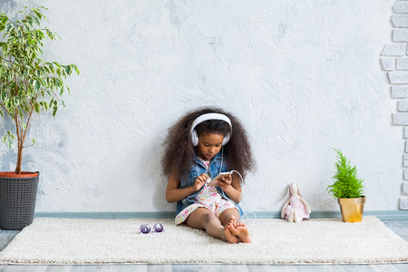cute African girl at home, listening to music in big white headphonesの写真素材