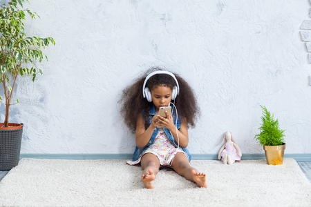 cute African girl at home, listening to music in big white headphonesの写真素材
