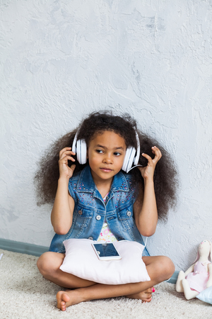 cute African girl at home, listening to music in big white headphonesの写真素材
