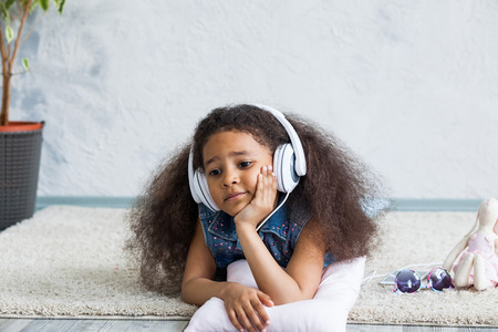 Bored African girl at home, listening to music in big white headphonesの写真素材