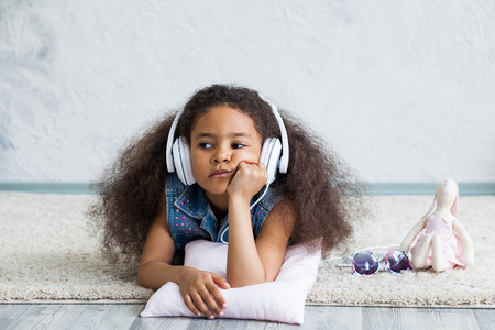 Bored African girl at home, listening to music in big white headphonesの写真素材