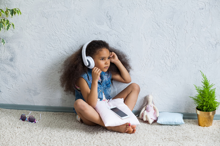 cute African girl at home, listening to music in big white headphonesの写真素材