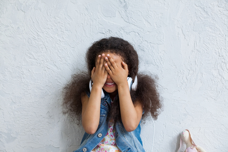 cute African girl listening to music in big white headphones, Closing her face with hands and smilingの写真素材