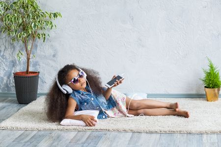 cute African girl at home, listening to music in big white headphonesの写真素材