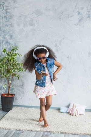 cute African girl at home, listening to music in big white headphones and dancingの写真素材