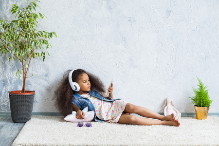 cute African girl at home, listening to music in big white headphonesの写真素材