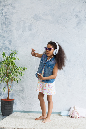 cute African girl at home, listening to music in big white headphones and dancingの写真素材