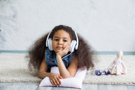 Bored African girl at home, listening to music in big white headphonesの写真素材
