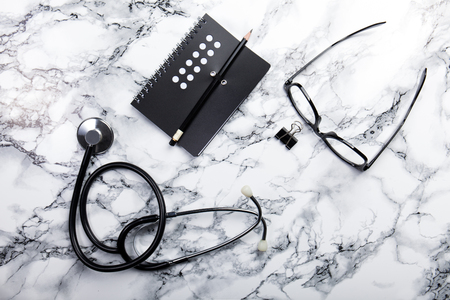 mininmal monochrome doctors office table desk workspace with diary plant stethoscope glasses keyboard pencil on black and white tableの写真素材