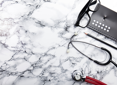 mininmal monochrome doctors office table desk workspace with diary plant stethoscope glasses keyboard pencil on black and white tableの写真素材