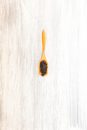 Composition of natural black tea with a leaves of rose. Macro photo of tea petals on a wooden spoon with a rose. Tea with the ingredients of flowers and tea located on a wooden Board.の写真素材