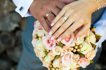 Close-up of hands of the groom and bride, against the background of a colorful bouquet.