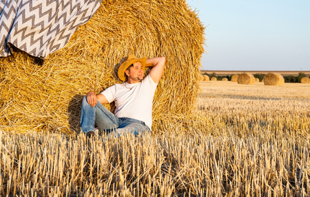 man wearing a straw hat resting after hay harvesting in haystacksの写真素材